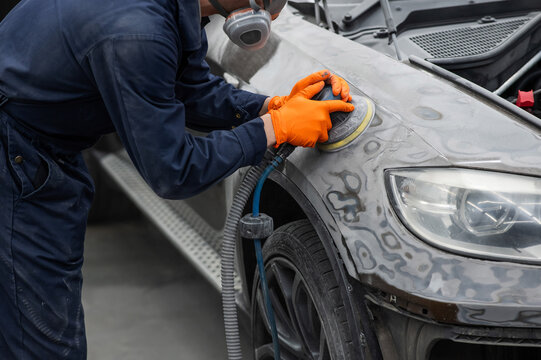 A mechanic sands the putty on a car body with a machine. Repair after an accident. 