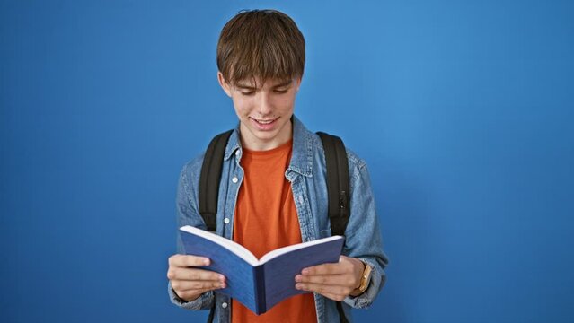 Blond teenager boy reads a book against a blue wall, depicting a casual, studious, and relaxed young man.