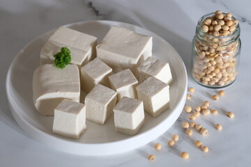 tofu or bean curd is traditional food made from soybean. sliced tofu on white plate on white marble table. tahu putih.