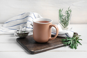 Board with cup of hot rosemary tea on white wooden table