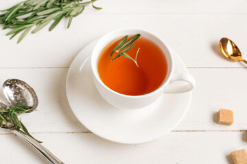 Cup of hot rosemary tea and sugar on white wooden background