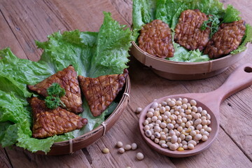 Tempe goreng, fried tempeh. Tempeh or tempe is traditional Indonesian food made from fermented soybeans. On lettuce at bamboo woven container on wooden table. Triangle shape tempeh. Super food. Vegan