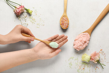 Female hands with wooden spoons of body scrubs and flowers on light background, closeup
