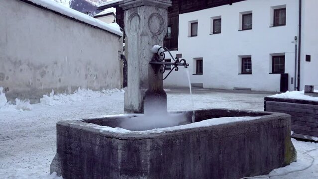 The village fountain in winter with running water and some light snow cover in the town center of Innichen - San Candido, South Tyrol, Italy