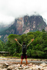 Obraz premium young adult person with backpack and arms raised looking at Angel Falls in Canaima National Park, Venezuela