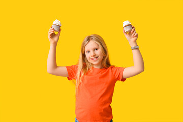 Cute little girl with delicious cupcakes on yellow background