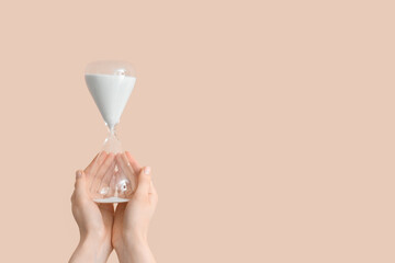 Female hands holding hourglass on beige background
