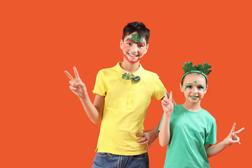 Funny kids with face paintings showing victory gestures on orange background. St. Patrick's Day...