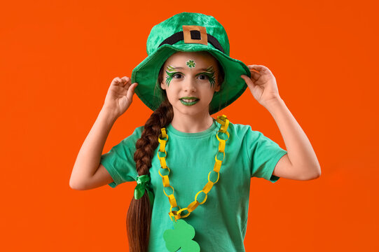 Funny girl with face painting and leprechaun's hat on orange background. St. Patrick's Day celebration