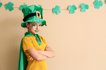 Funny girl with face painting, cape and leprechaun's hat near beige wall. St. Patrick's Day celebration