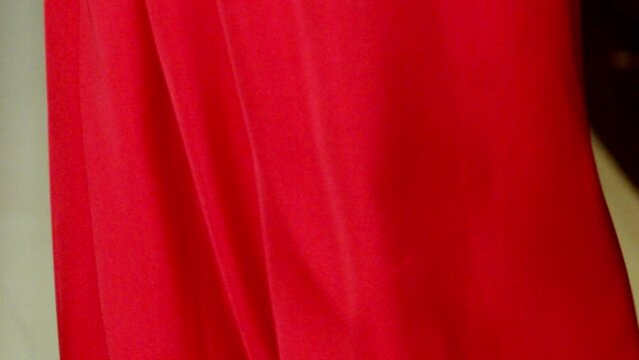 With red fabric dress flowing, stunning model tends to her hair. Slow-mo
