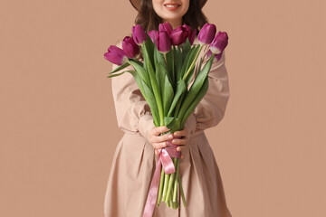 Young woman with bouquet of beautiful purple tulips on brown background