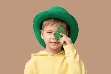 Cute little boy in leprechaun hat with clover on brown background. St. Patrick's Day celebration