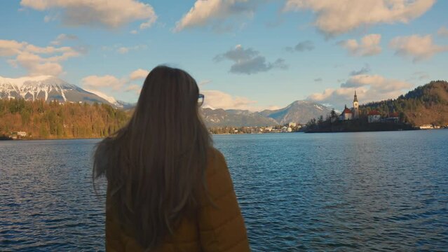 4K video of a beautiful young caucasian female looking over at the island with the church on it. Very famous touristic destination in Bled, Slovenia.