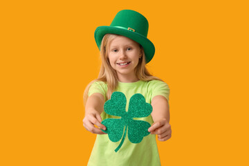 Cute little girl in leprechaun hat with clover on yellow background. St. Patrick's Day celebration