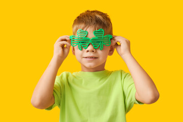 Cute little boy in decorative glasses in shape of clover on yellow background. St. Patrick's Day...