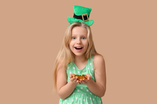 Cute little girl in leprechaun hat with coins on brown background. St. Patrick's Day celebration