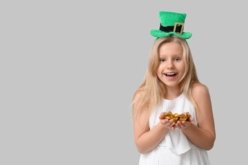 Cute little girl in leprechaun hat with coins on grey background. St. Patrick's Day celebration