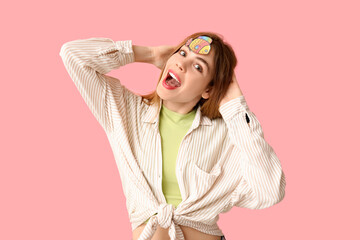 Beautiful young happy woman with paper fish attached to her forehead on pink background. April Fools Day celebration - obrazy, fototapety, plakaty