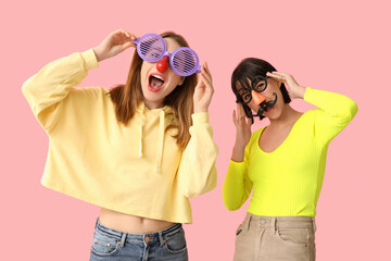 Beautiful young women in funny disguise on pink background. April Fools Day celebration