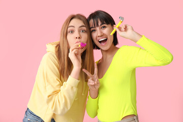 Beautiful young women with party whistles on pink background. April Fools Day celebration