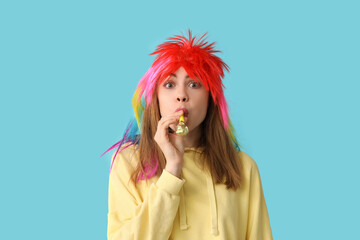 Beautiful young woman in funny clown disguise with party whistle on blue background. April Fools Day celebration