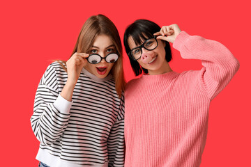 Beautiful young shocked women in funny disguise on red background. April Fools Day celebration