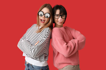 Beautiful young women in funny disguise on red background. April Fools Day celebration