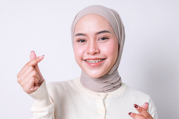 Closeup of young Asian woman with dental braces and hijab showing mini heart sign isolated on white...