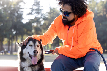 Mexican man with curly hair, petting his husky dog in a park in Mexico City