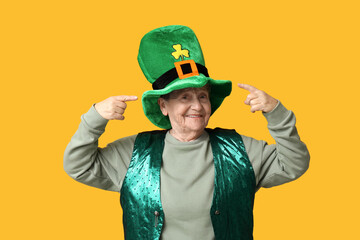 Senior woman pointing at leprechaun hat on yellow background. St. Patrick's Day celebration