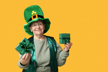Senior woman in leprechaun hat with gift boxes on yellow background. St. Patrick's Day celebration