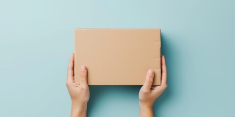 Top view to female hands holding empty brown cardboard box on light blue background. Mockup parcel box. Packaging, shopping, delivery concept - obrazy, fototapety, plakaty
