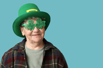 Senior woman in leprechaun hat and decorative glasses in shape of clover on blue background. St....