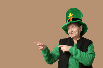 Senior woman in leprechaun hat pointing at something on brown background. St. Patrick's Day celebration