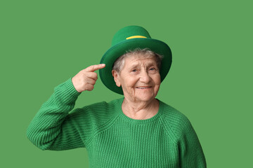 Senior woman pointing at leprechaun hat on green background. St. Patrick's Day celebration