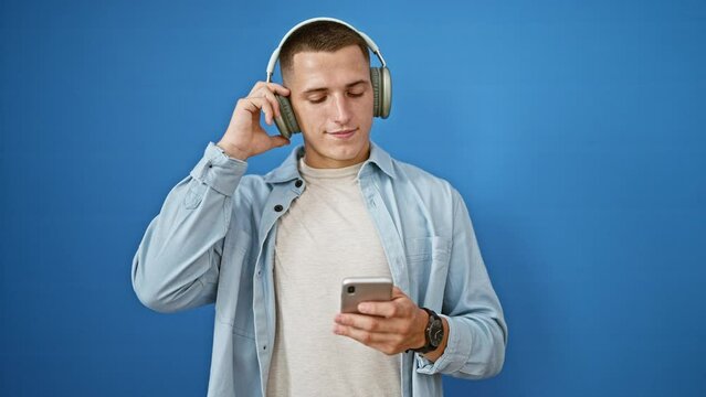 Young hispanic man wearing headphones and using smartphone against blue background