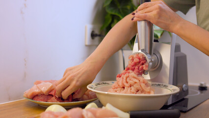 A young woman makes minced meat in a meat grinder