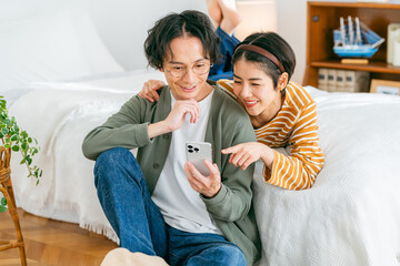くつろぎながらスマホを見る若い日本人カップル