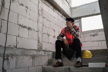 Young Asian male construction worker staff feeling sad and upset while sitting on the floor of the...