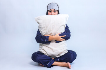 Full body of woman sitting in pajamas and sleep eye mask holding and hugging pillow