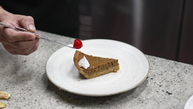 The pastry chef and his apprentice prepares recipe for a slice of pumpkin brownie cream pie dessert with cream and cherry