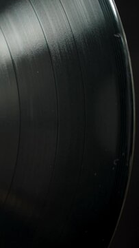 A black vinyl record slowly rotates, top view, close-up.