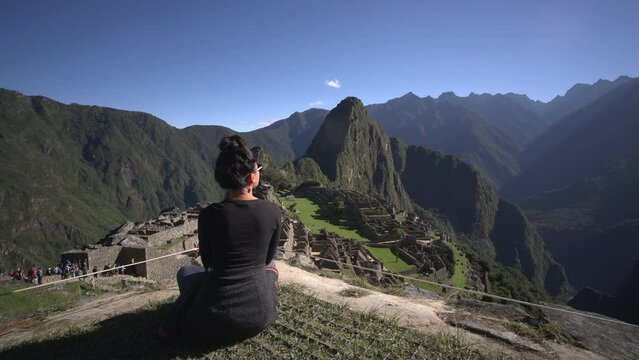An asian woman admiring the view of the majestic Macchu Picchu in Peru right in front of her. As seen, the dazzling architectural beauty seems to impress her.