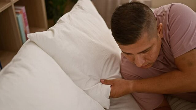 Handsome young latin man resting in comfort on his cozy bed, relaxing and ready to sleep in his apartment's bedroom interior