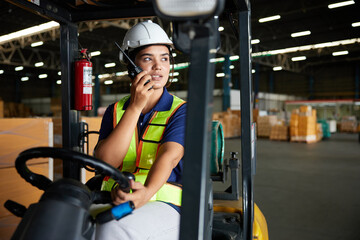 Indian worker driving a forklift and using walkie talkie in warehouse storage