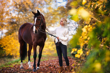 Young blonde girl with her horse walking through a colorful autumn forest.