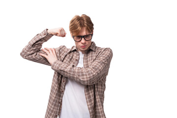 young stylish european student man with golden hair in glasses and a plaid shirt shows muscles