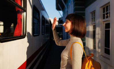 young traveler with a backpack stands on the platform and says goodbye, saying goodbye before...