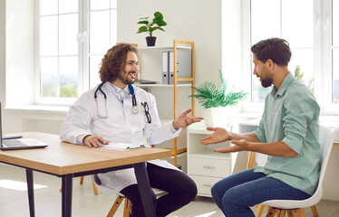 Fototapeta premium Medicine, healthcare and people. Friendly doctor advises man on health maintenance and gives advice on treatment. Man in medical coat sitting in office in clinic is talking to joyful male patient. 